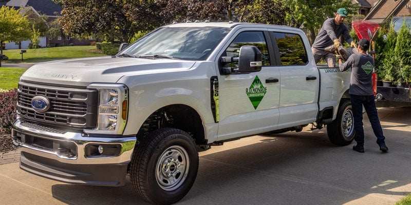 Two men load landscaping supplies into the back of a white Ford Super Duty truck with an R.D. Monroe Landscaping logo.