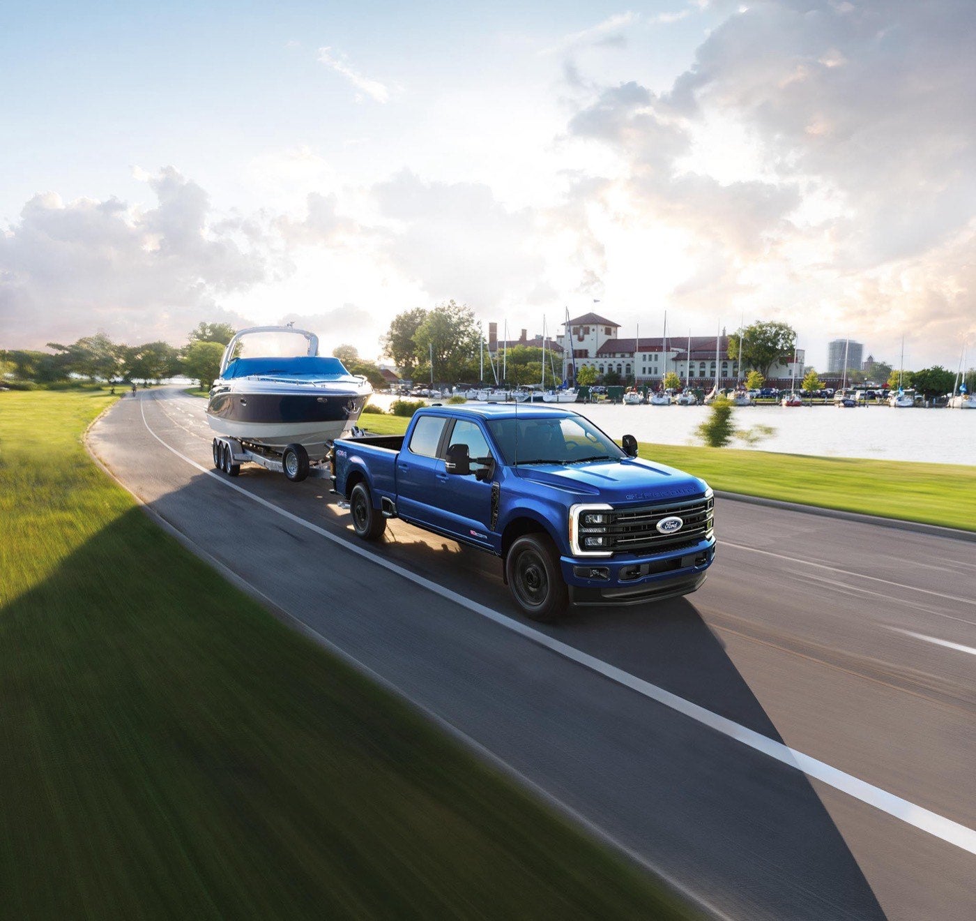 Blue Ford Super Duty pickup towing a boat on a trailer along a waterfront road